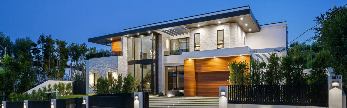 modern two-story house with a wooden garage door, large windows, and exterior lighting at dusk